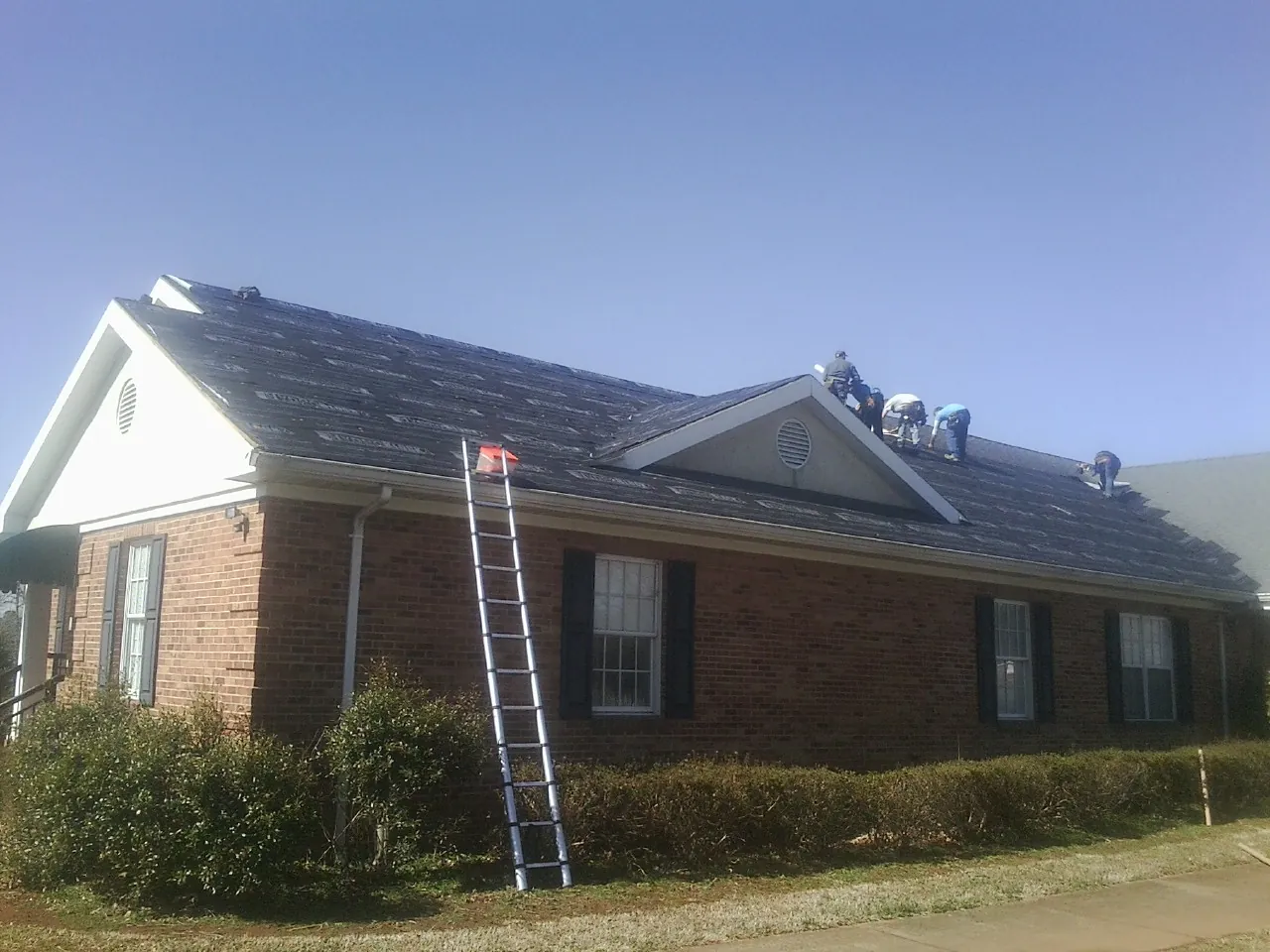 Crew tearing shingles off a brick ranch roof with a ladder set — Emergency Roof Repair work by our crew in Stuart