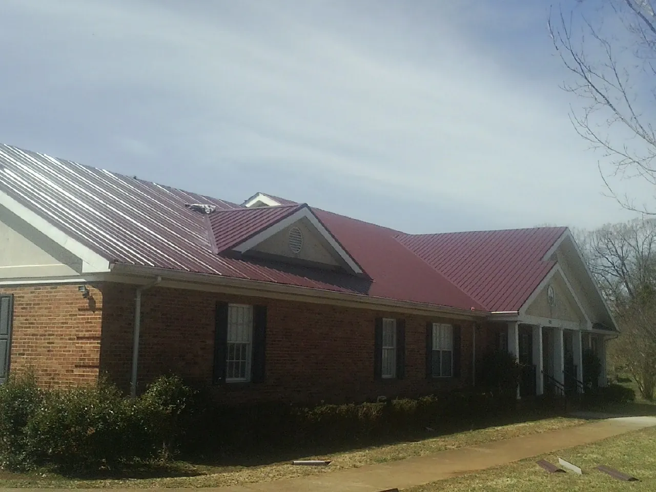 Red metal roof with gabled entries on a long brick building, from a Hail Damage Roof Repair job in Stuart